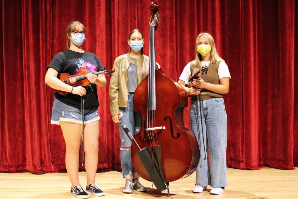 Pictured from left are John Marshall High School Strings students Megan Huff, Grace Gatts and Sofiah Bozenske, who are standing in front of a red curtain while holding their violins.