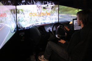 Collision is on the video screen windshield. Pictured is JMHS junior Rhyder Dunn who just collided, virtually, with a car when driving on a rural road of West Virginia. This happened while he was in the driver’s seat of the WV ABCA DUI Simulator.